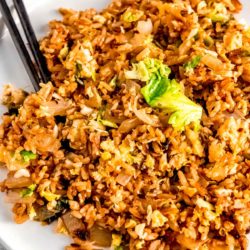 a white plate piled high with brussels sprout fried rice with chopsticks