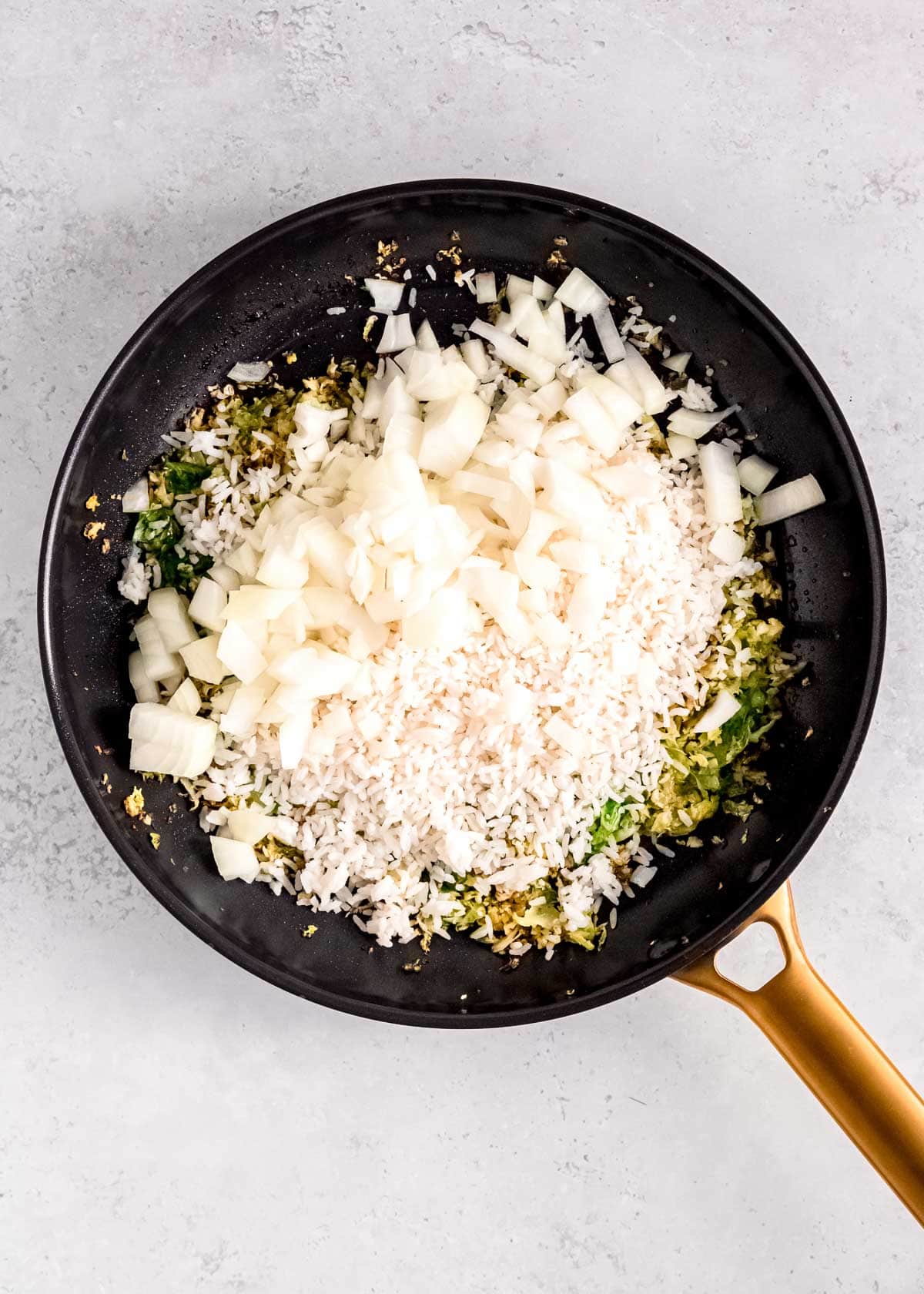 diced onion added to a hot skillet with cold rice and sauteed brussels sprouts and garlic