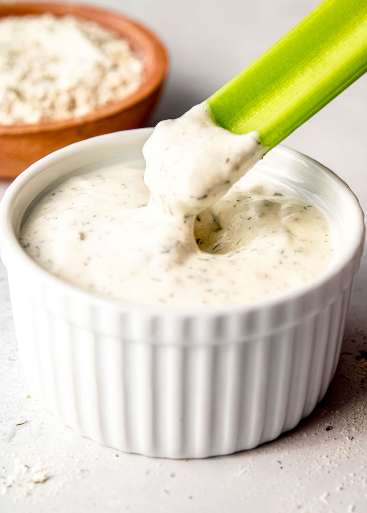 image of celery stick being dipped in ranch dressing in a white bowl