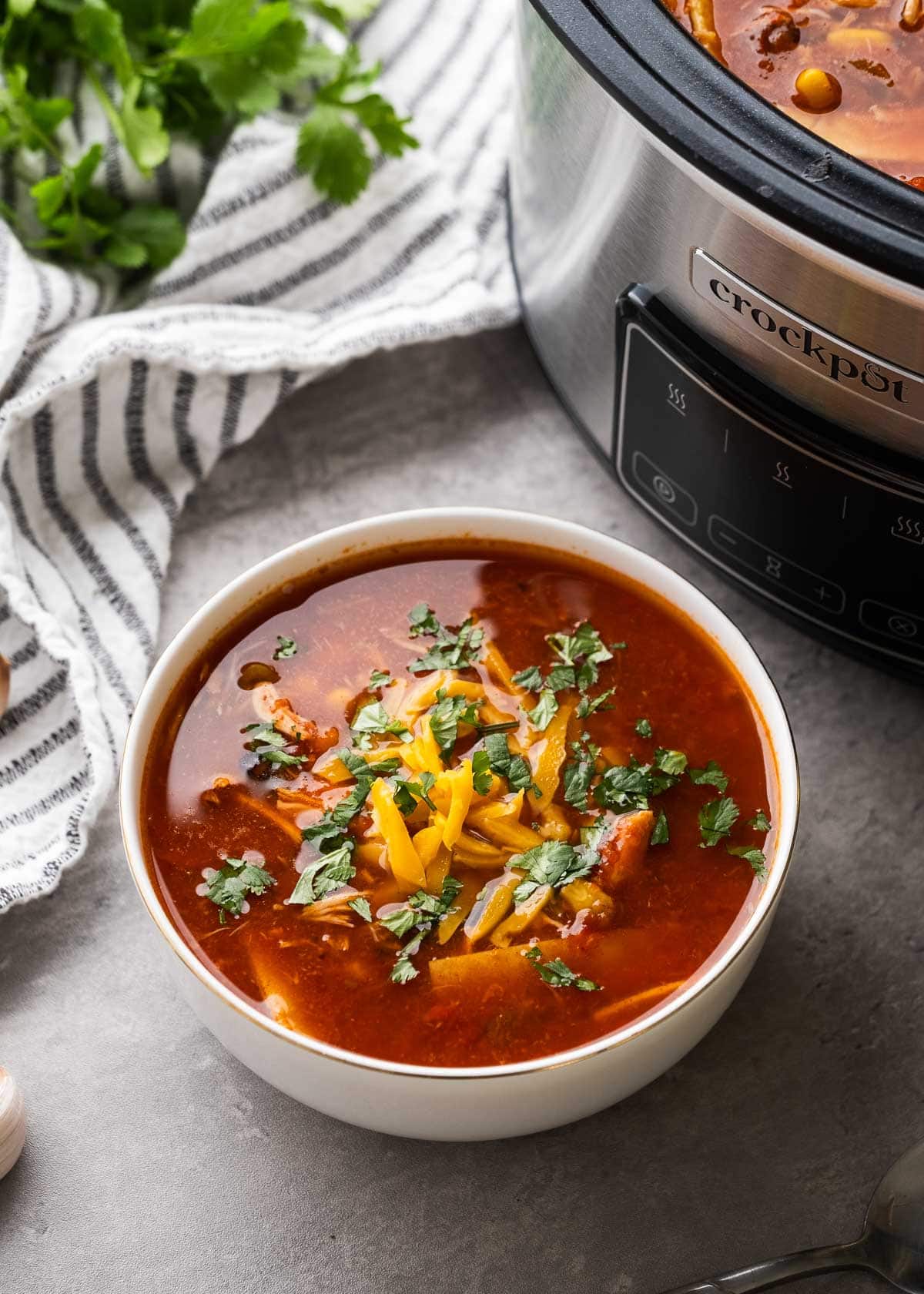a big bowl of slow cooker enchilada soup beside a crock pot