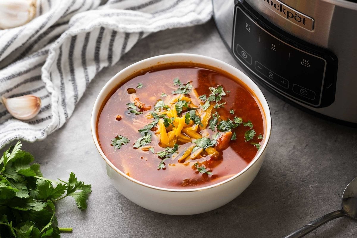 red enchilada soup full of chicken, beans, and tomatoes, topped with cheese and cilantro