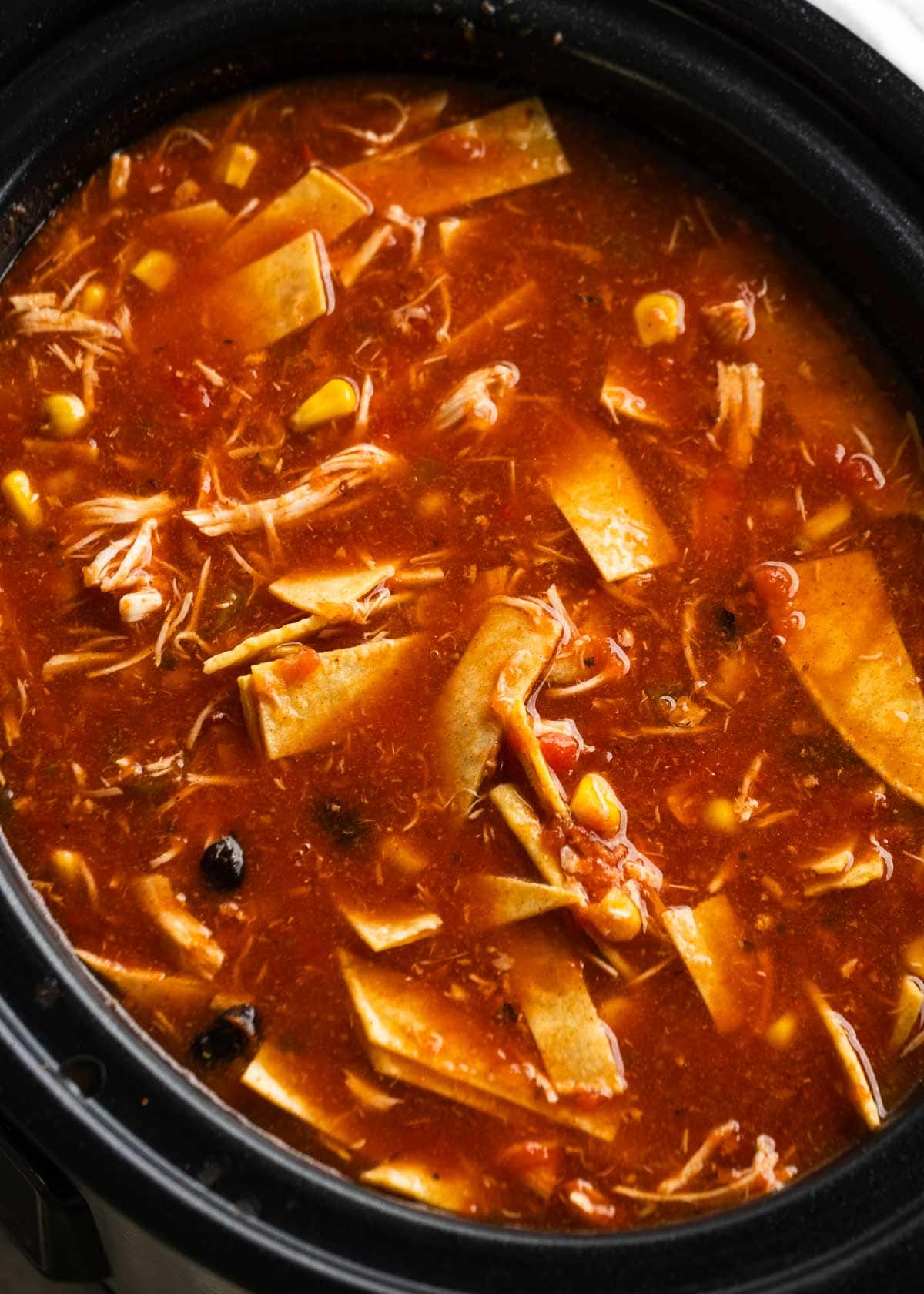 strips of corn tortillas added into chicken enchilada soup in a crockpot