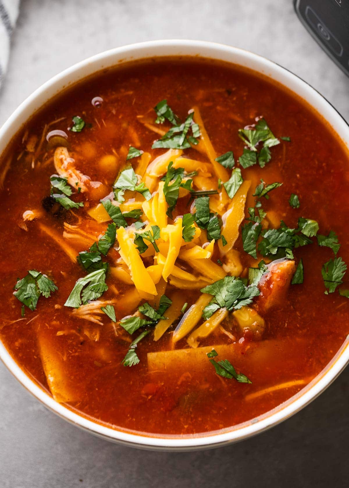 a white bowl with chicken enchilada soup topped with cheese and cilantro