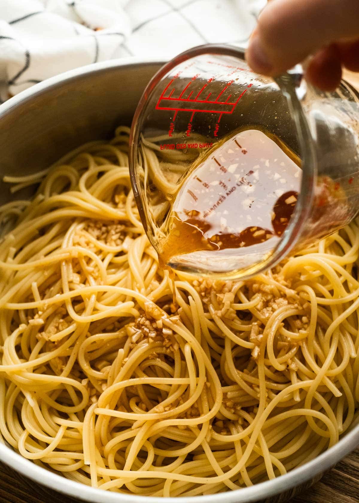 tasty sauce being poured over cooked spaghetti noodles in a bowl