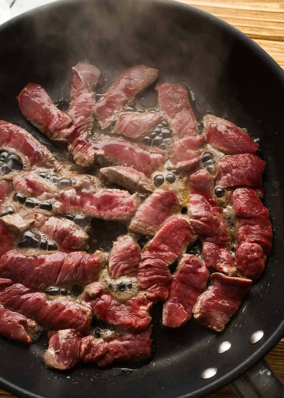 steak strips cooking in a skillet on the first side