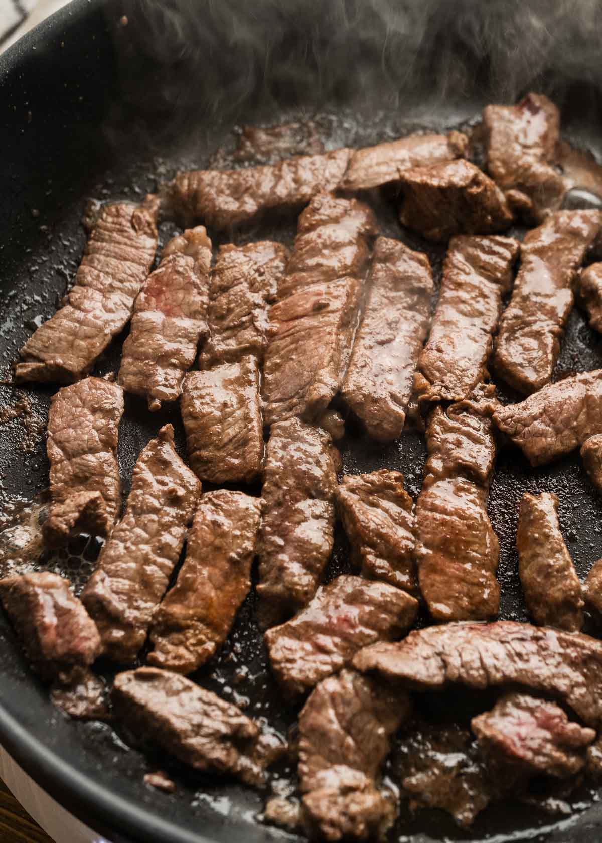 steak strips browning on their second side in a skillet