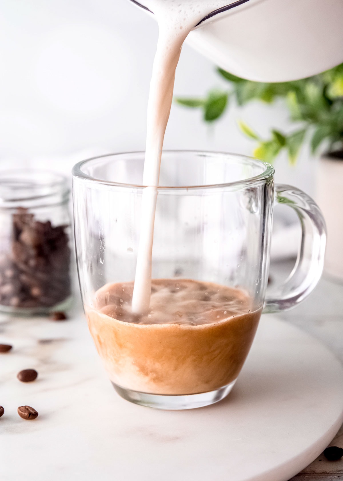 frothed milk being added to clear coffee mug