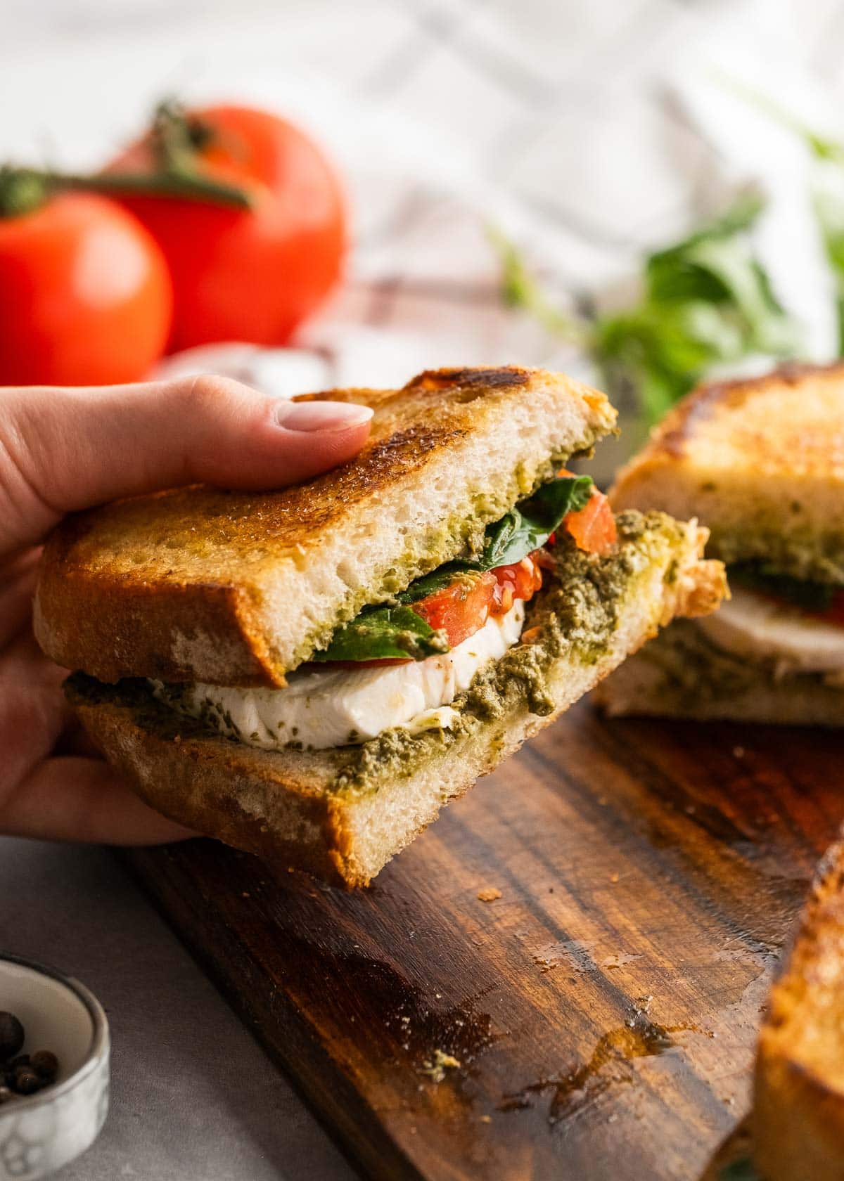 caprese sandwich being held up cutting board