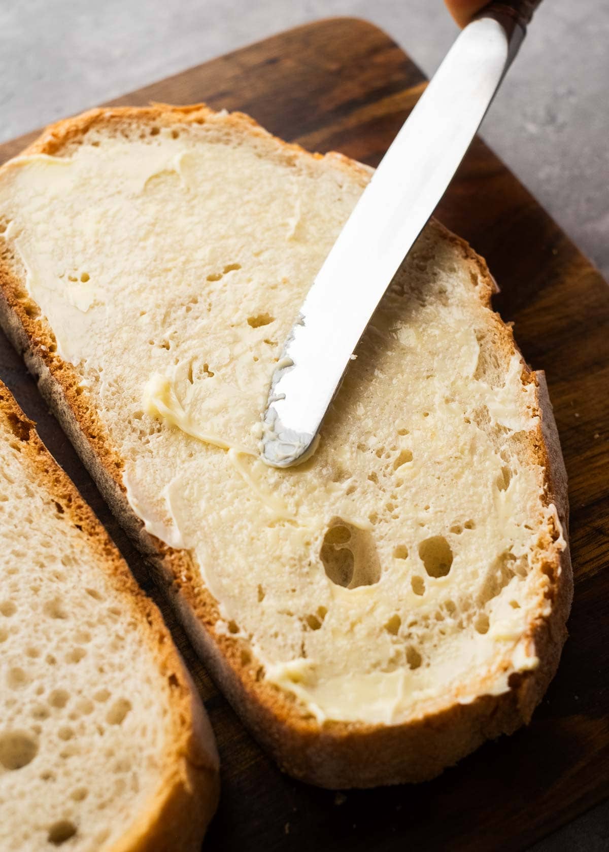 bread being buttered on wooden cutting board