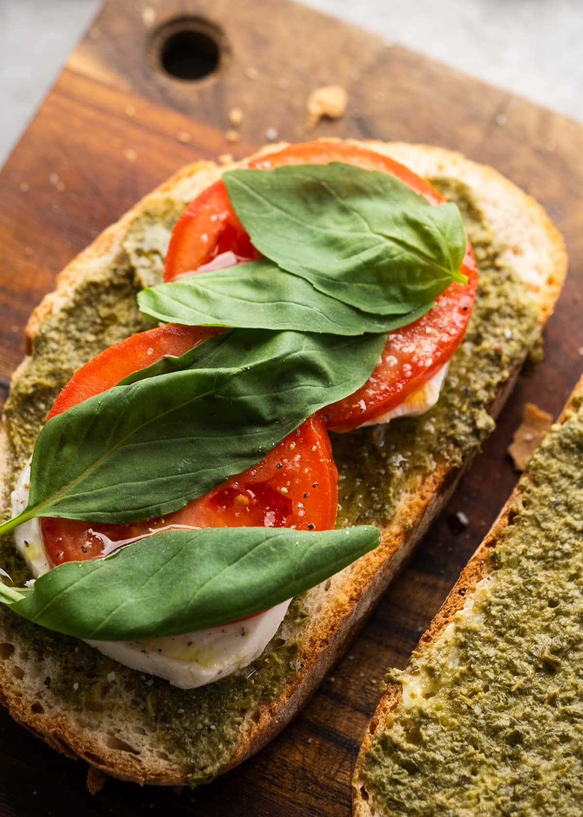tomato and basil being added to sliced bread on wooden cutting board