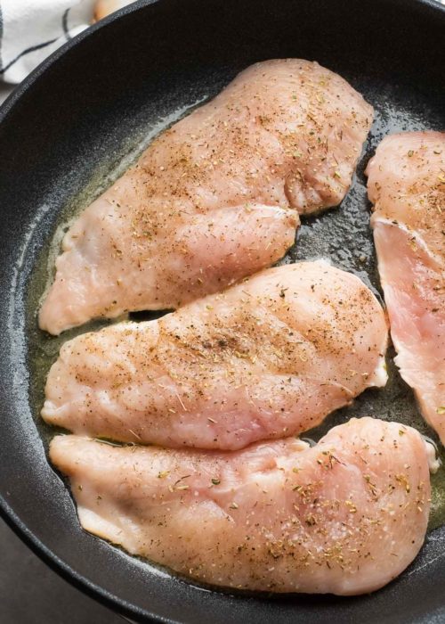 four seasoned chicken breasts searing in a cast iron skillet with butter.