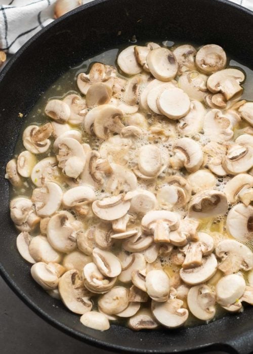 mushrooms, garlic, and chicken broth added to a skillet to make a mushroom sauce for the chicken