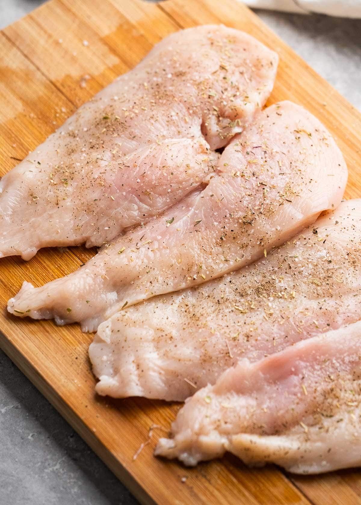 thinly-pounded chicken thighs seasoned with salt, pepper, and italian seasoning on a cutting board