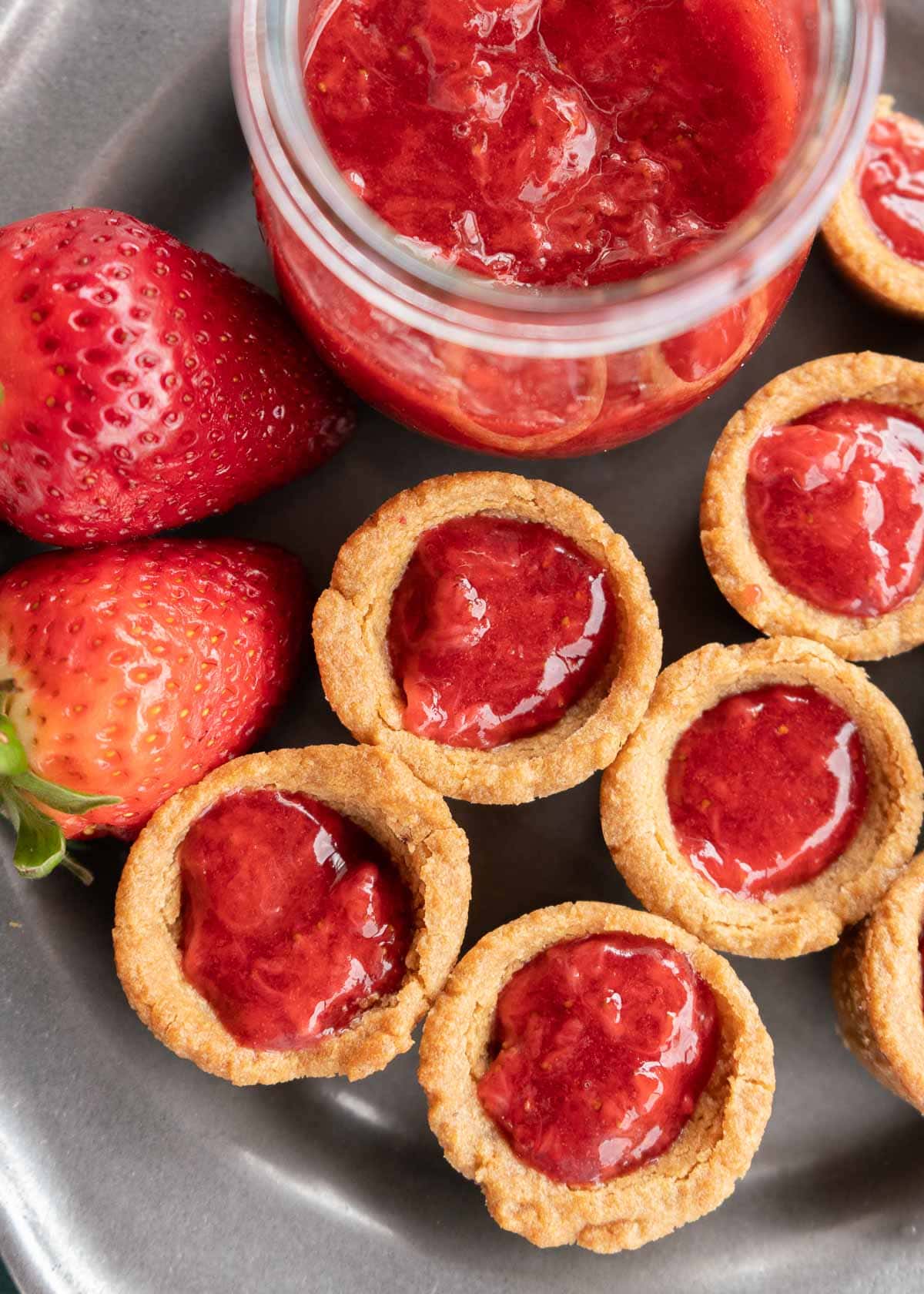 peanut butter and jelly cookie cups on a plate with strawberries and sugar-free sauce on a plate
