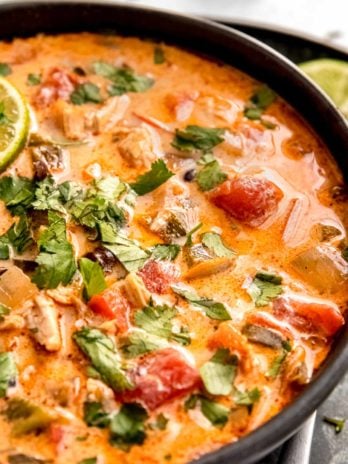 closeup view of a dark bowl of creamy chicken poblano soup garnished with fresh herbs and a lime slice