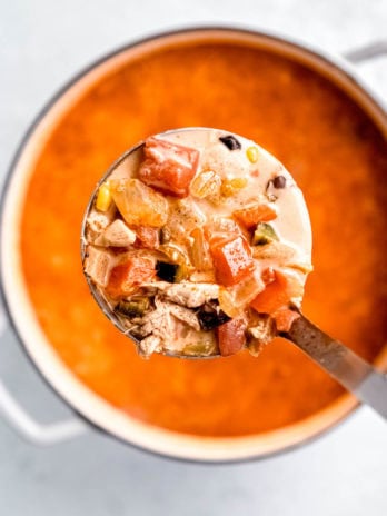 a ladle full of chicken, peppers, and broth over a pot of poblano chicken soup