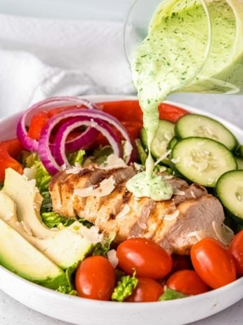 green goddess dressing being poured on chicken on white plate
