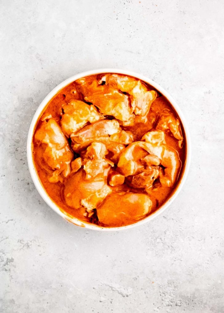 chicken thighs being marinated in white bowl
