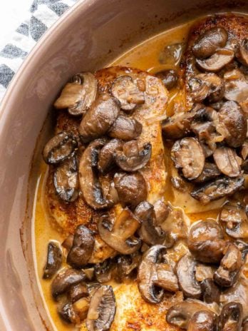 four chicken breasts in a skillet smothered in creamy mushroom sauce