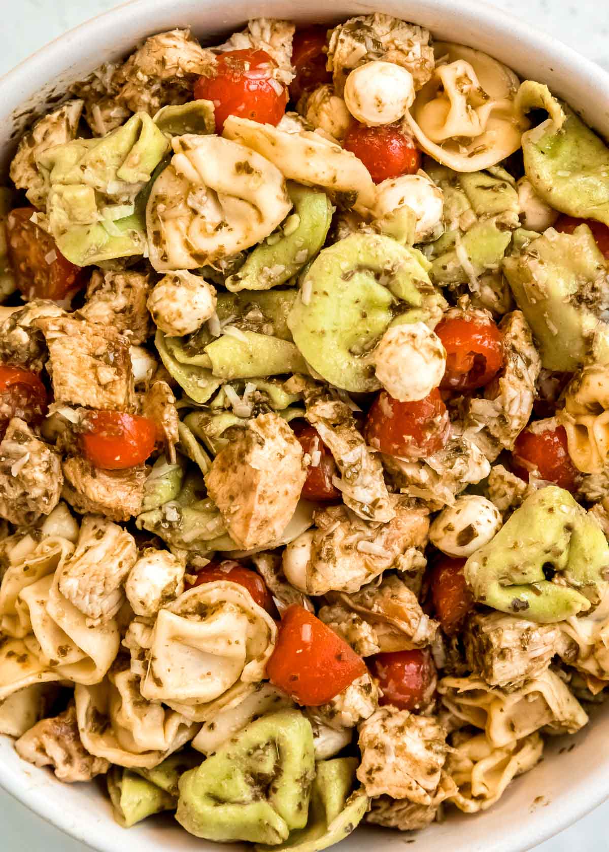 closeup shot of tortellini pasta salad with pesto, mozzarella, and tomatoes.