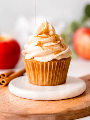 caramel syrup being drizzled onto a gluten-free apple cinnamon cupcake topped with caramel buttercream
