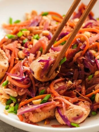 chopsticks holding a bite of chicken in a white dish full of egg roll in a bowl