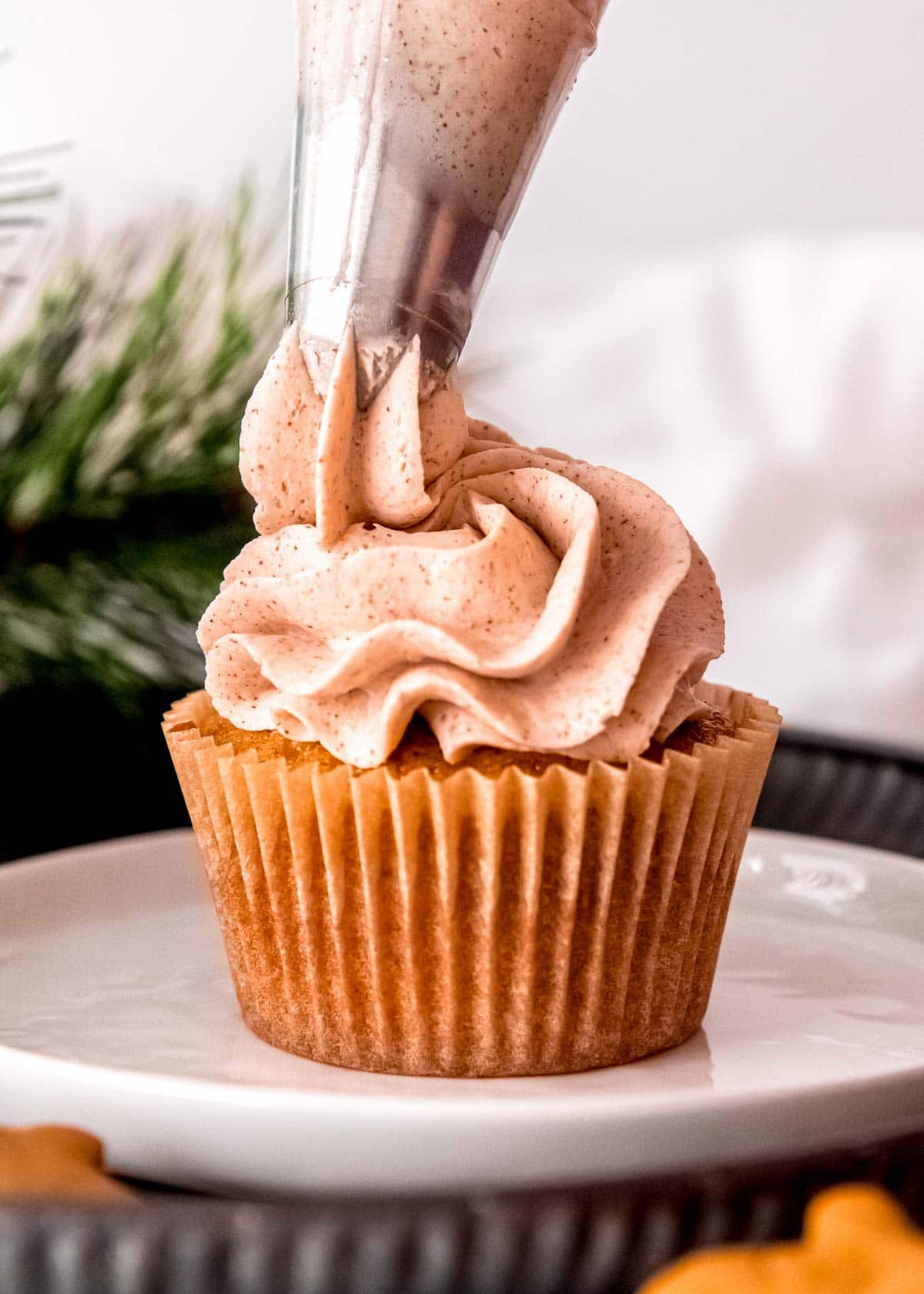 cinnamon buttercream frosting being piped onto a gluten-free gingerbread cupcake