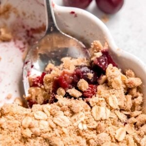 a spoon scooping a serving of classic cherry crisp with a crumbled oat topping