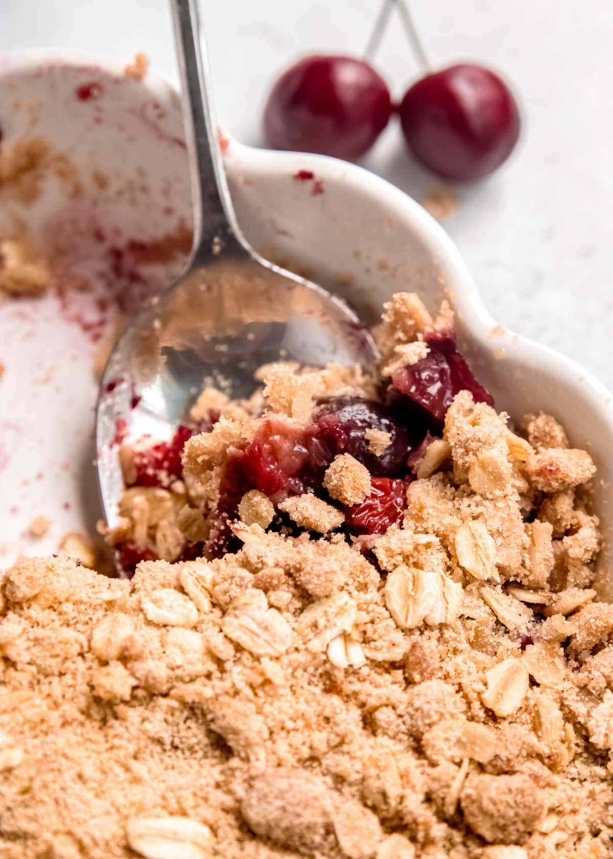 a spoon scooping a serving of classic cherry crisp with a crumbled oat topping