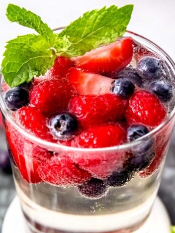 a glass full of white sangria topped with fresh berries and mint