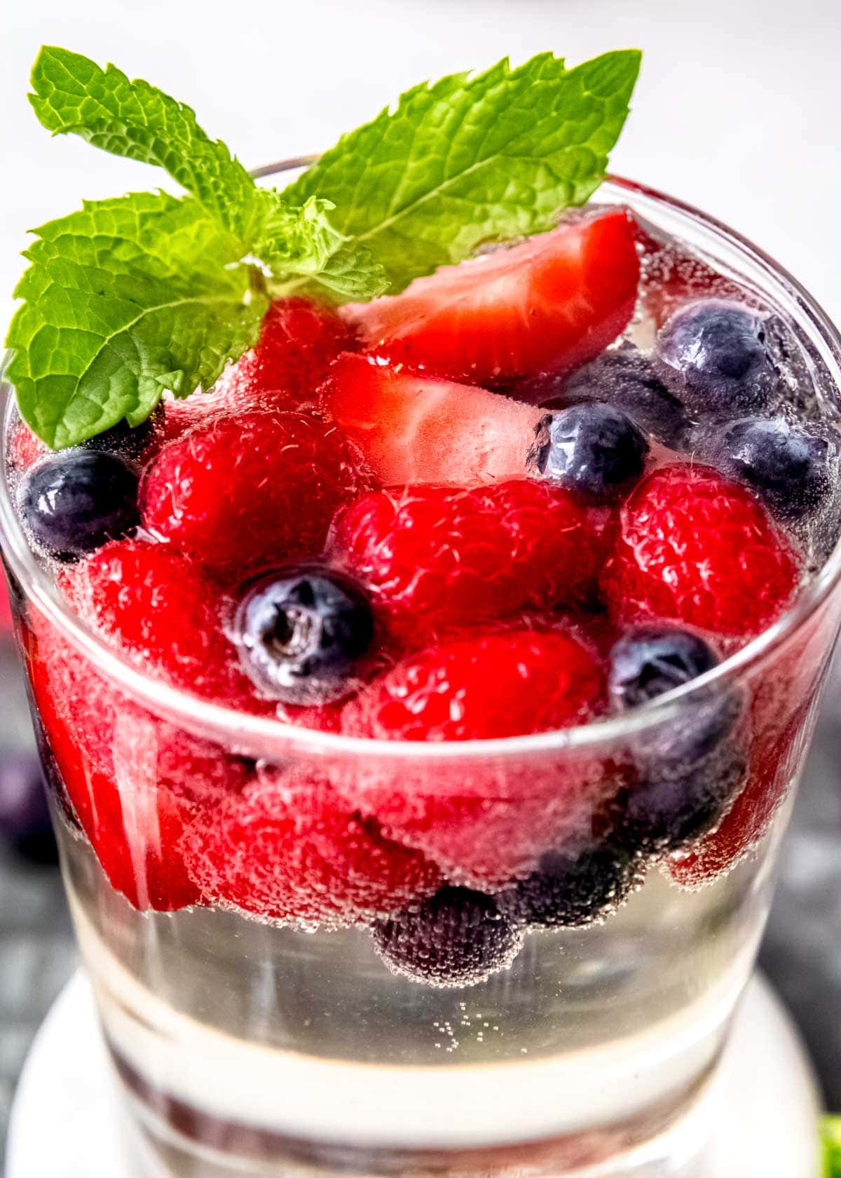 a glass full of white sangria topped with fresh berries and mint