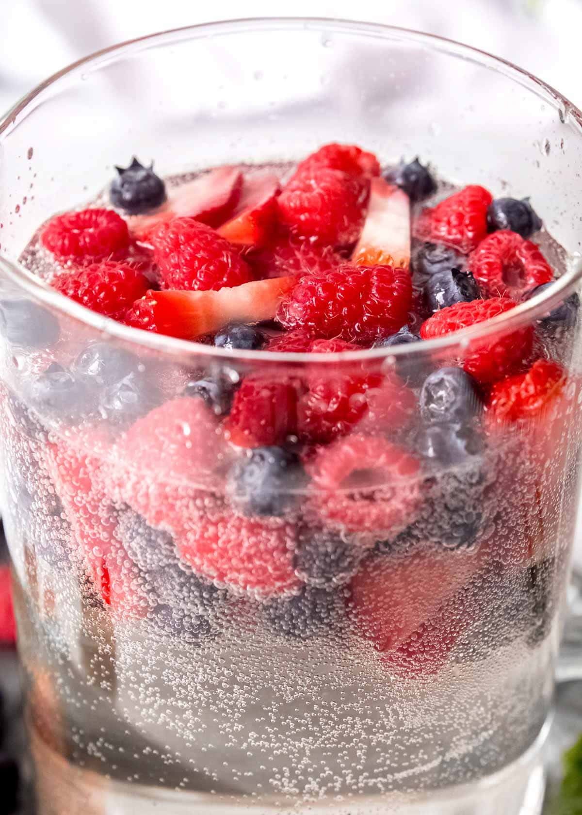 closeup shot showing raspberries, strawberries, and blueberries in a bubbly white sangria