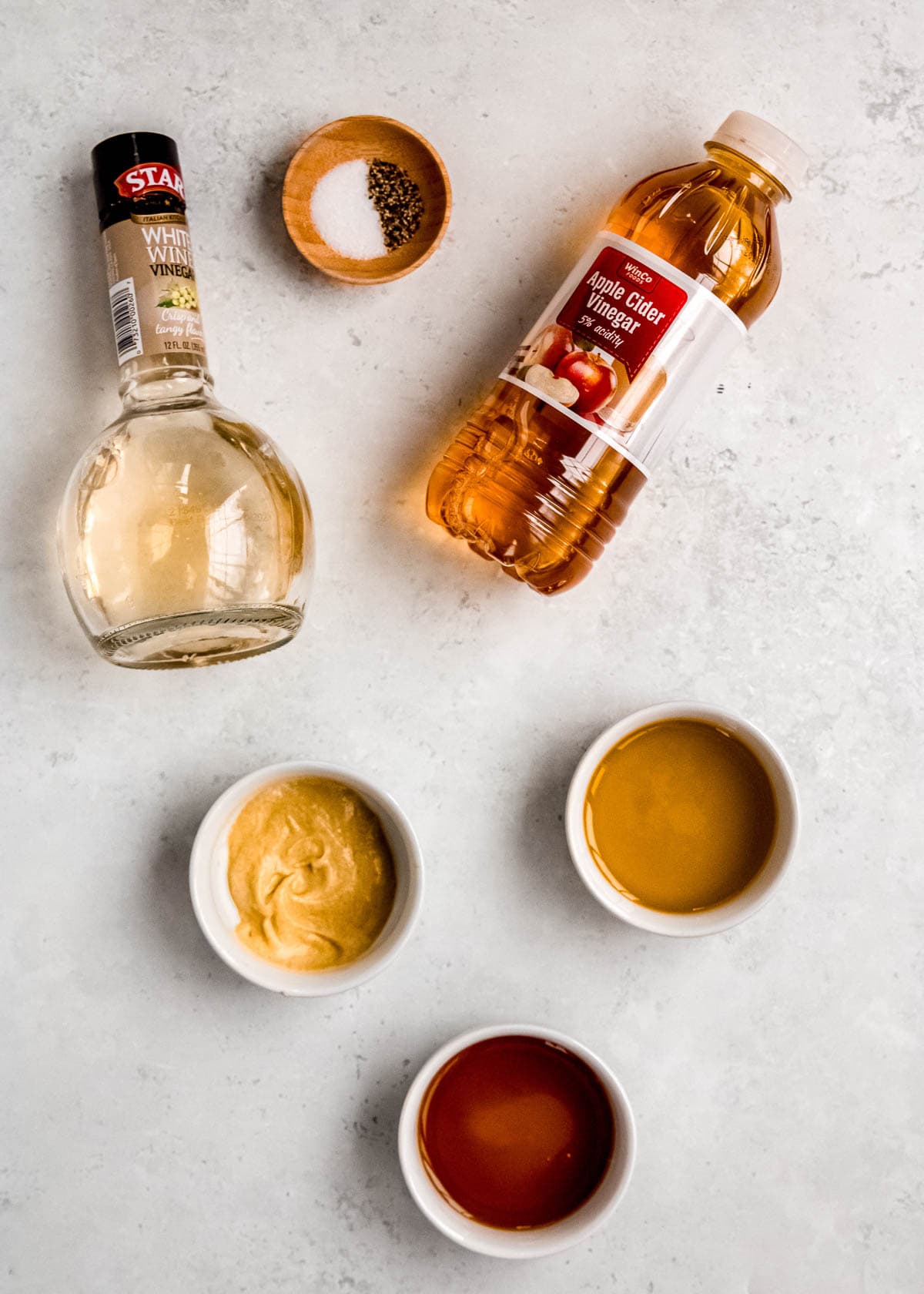 apple cider vinegar, white wine vinegar, dijon mustard, salt, pepper, olive oil, and maple syrup on a countertop for maple-dijon dressing