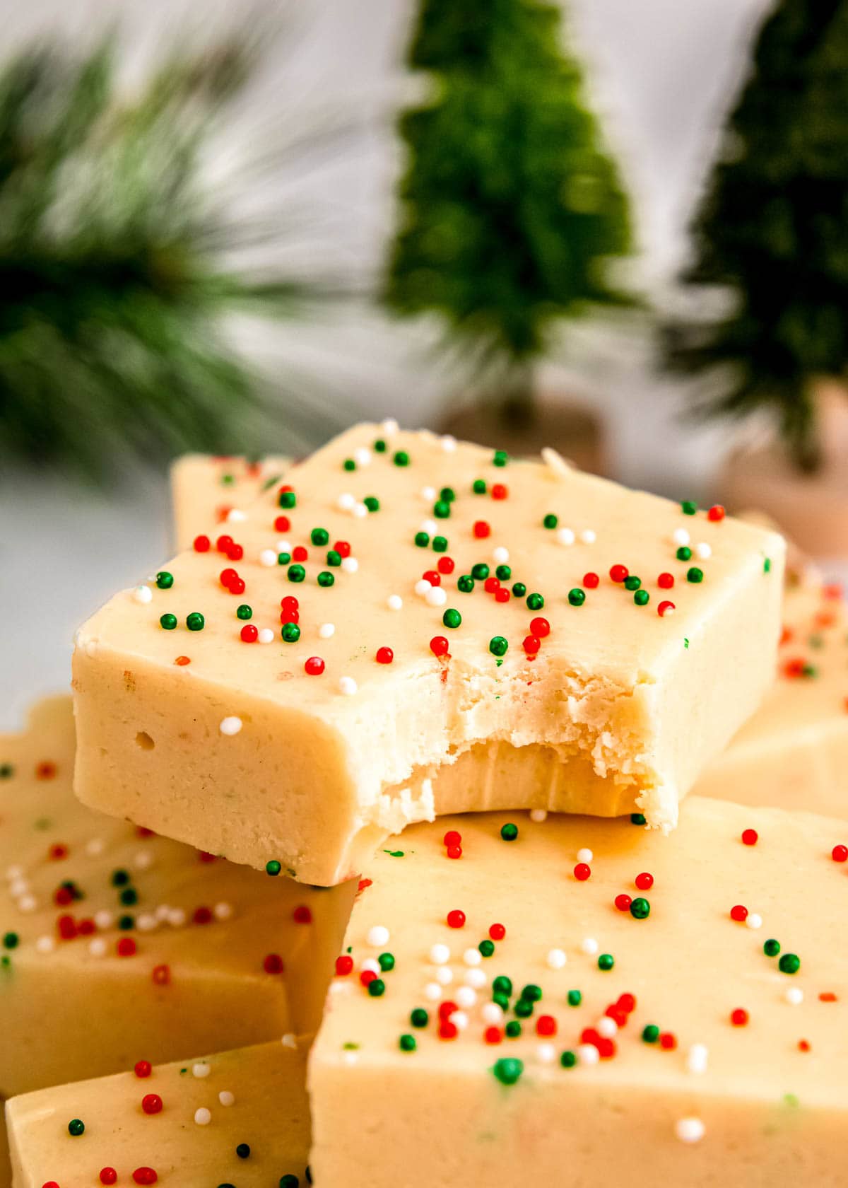 a bite taken out of creamy sugar cookie fudge in front of a holiday background