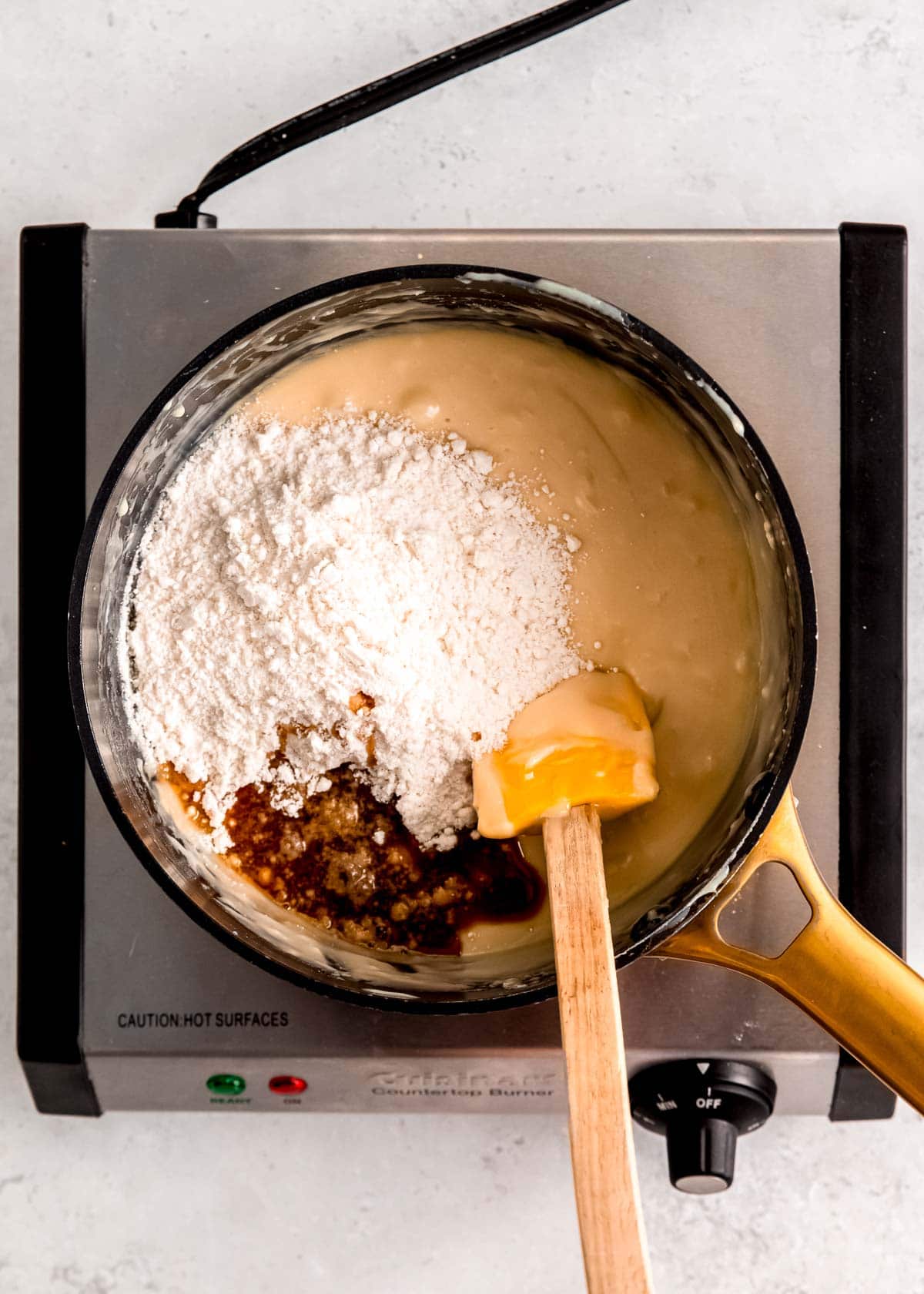 heat treated sugar cookie dough, almond extract, and vanilla extract being stirred into a white chocolate mixture in a saucepan