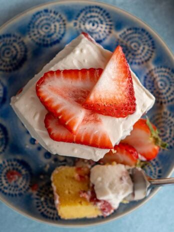 overhead shot showing sliced strawberries atop fluffy whipped cream cheese frosting on a strawberry poke cake