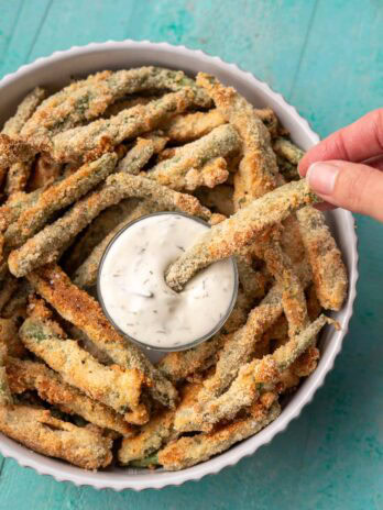 a hand dipping a gluten-free green bean fry into ranch dressing