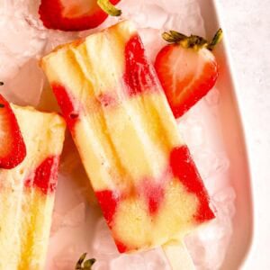 several strawberry popsicles on ice with half strawberries around