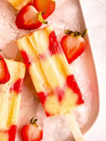 several strawberry popsicles on ice with half strawberries around