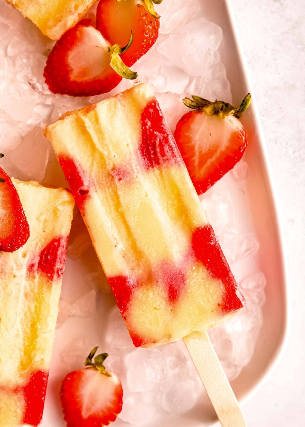 several strawberry popsicles on ice with half strawberries around