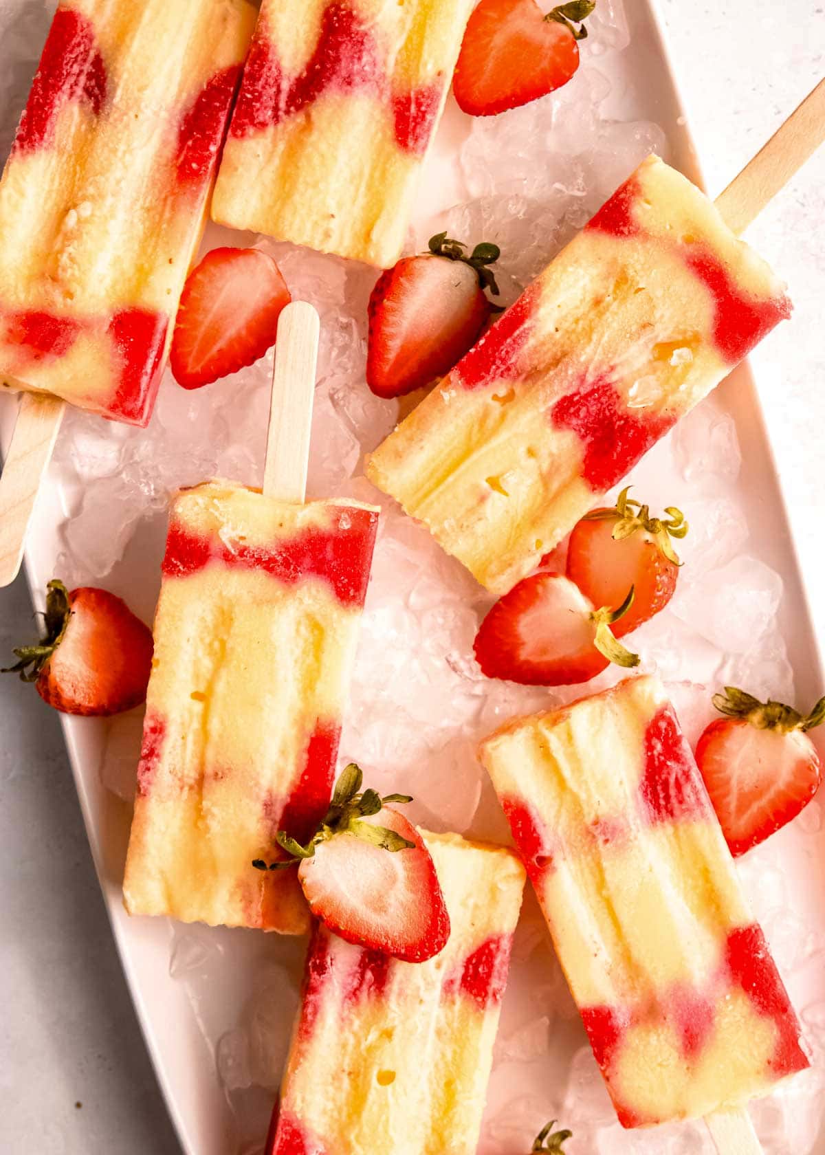 six strawberry popsicles on a bed of ice with halved strawberries