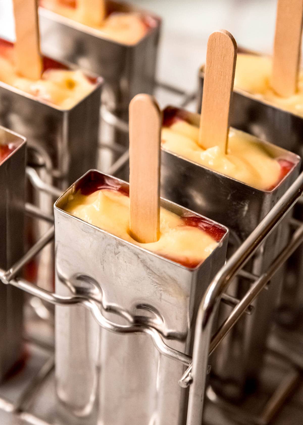 a popsicle mold filled with vanilla pudding and strawberry puree with a popsicle stick in the middle