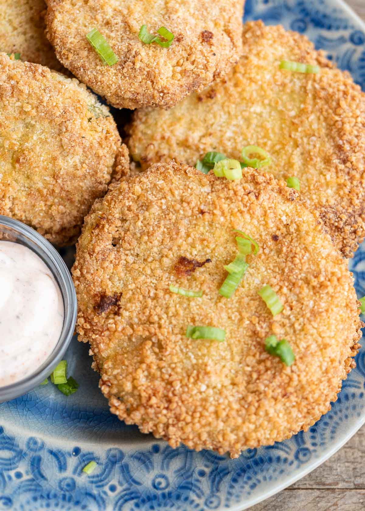 a blue plate full of crispy air fryer fried green tomatoes with a side of dipping sauce