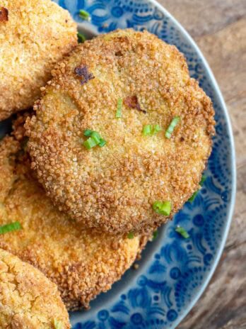 several fried green tomatoes on a blue platter, topped with chopped green onions
