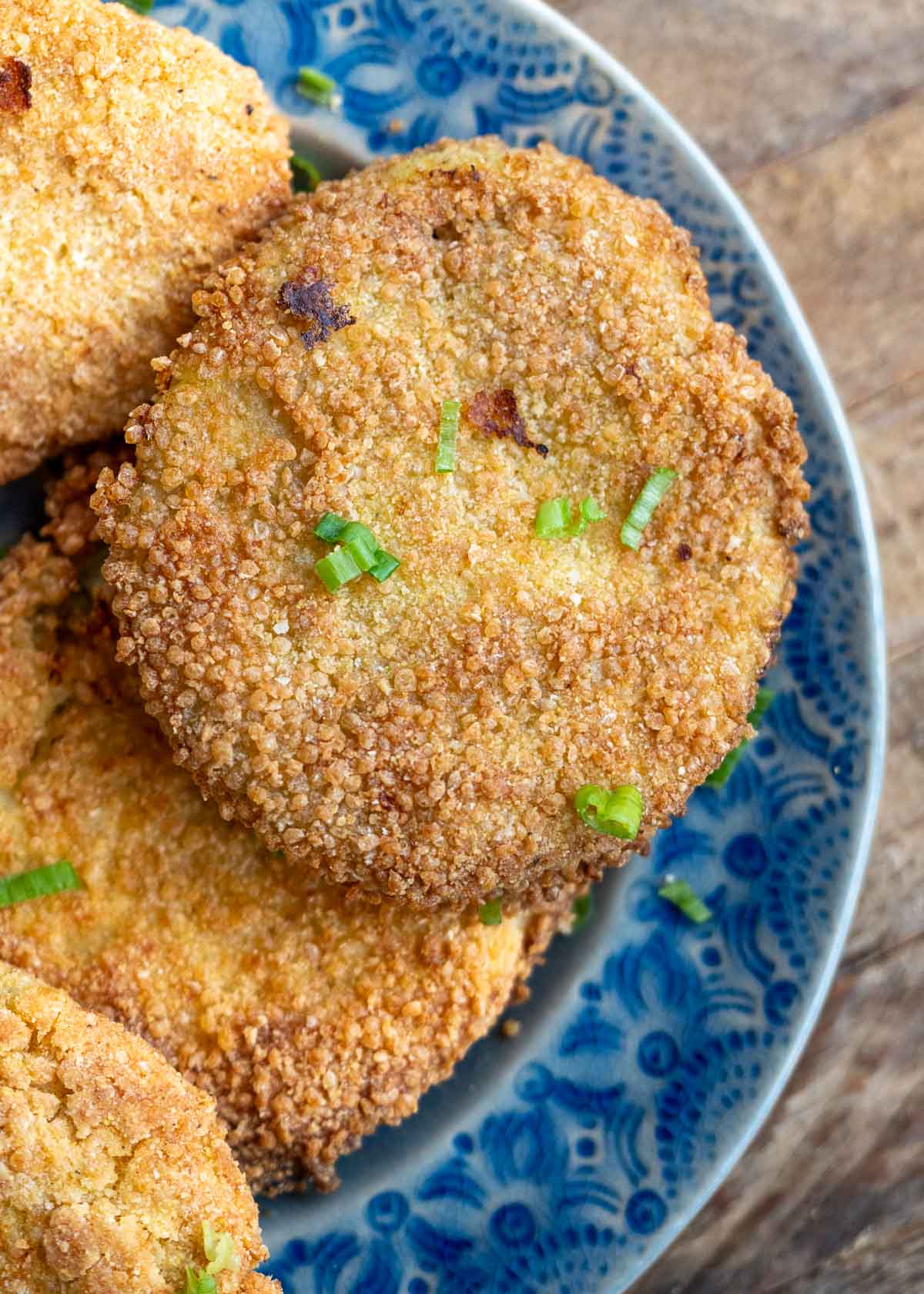 several fried green tomatoes on a blue platter, topped with chopped green onions