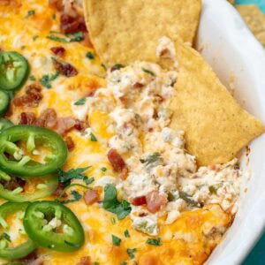 a white bowl filled with creamy jalapeno popper dip with bacon, jalapenos, cheese, and tortilla chips