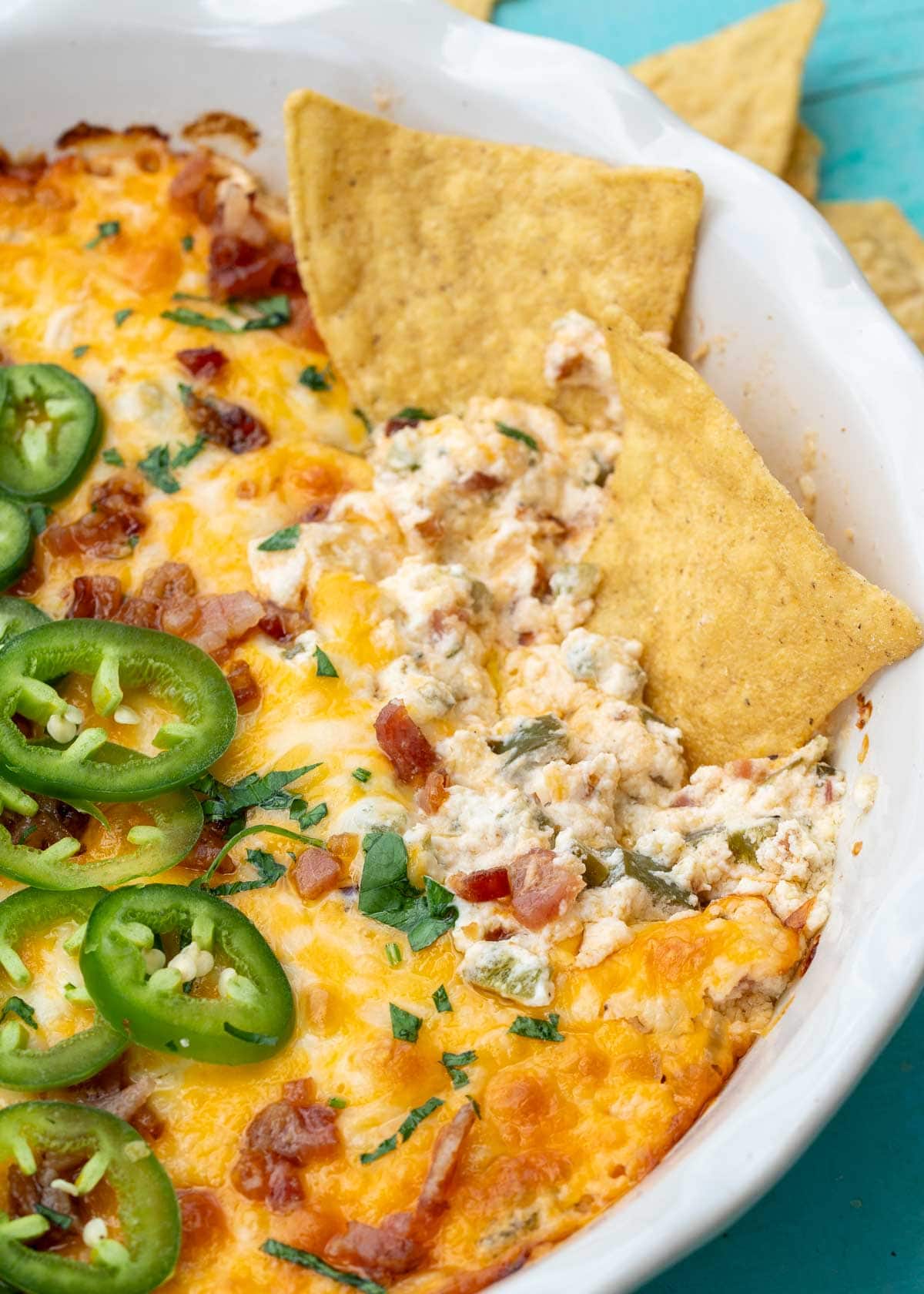 a white bowl filled with creamy jalapeno popper dip with bacon, jalapenos, cheese, and tortilla chips
