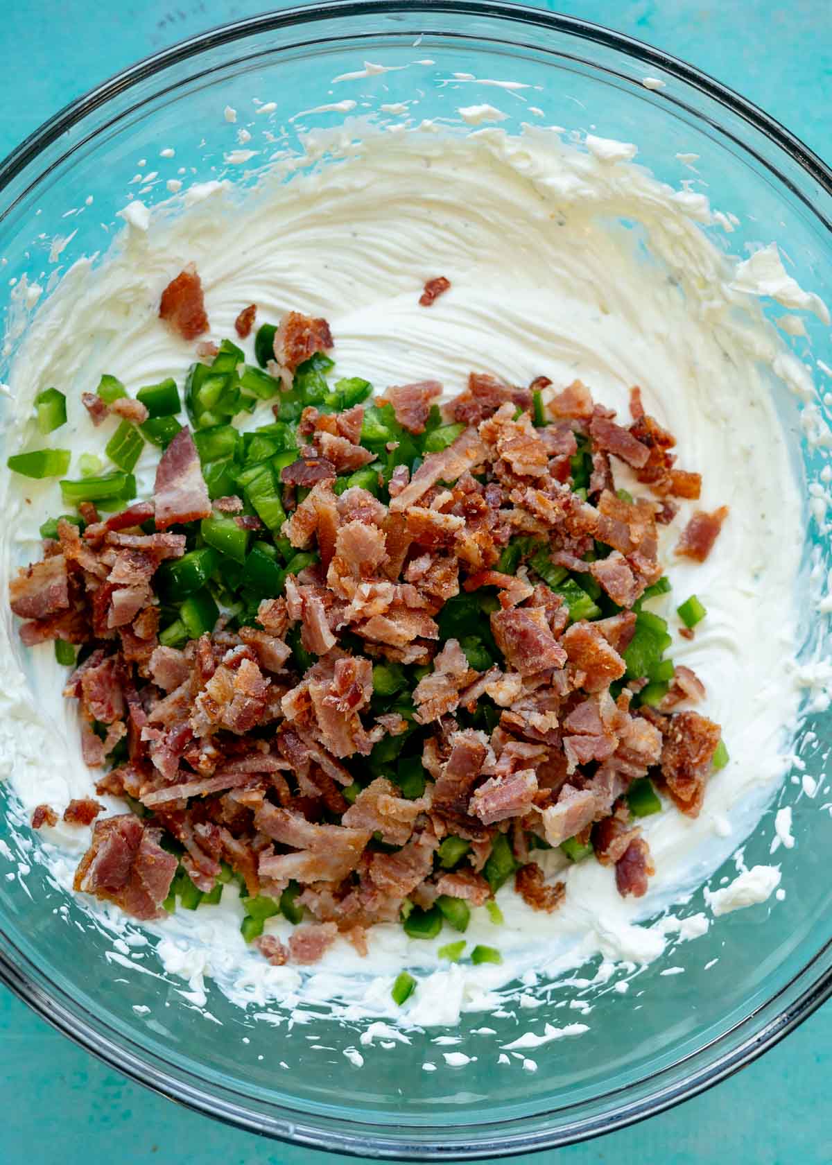 bacon and jalapenos being added to a creamy mixture of sour cream, mayonnaise, and cream cheese