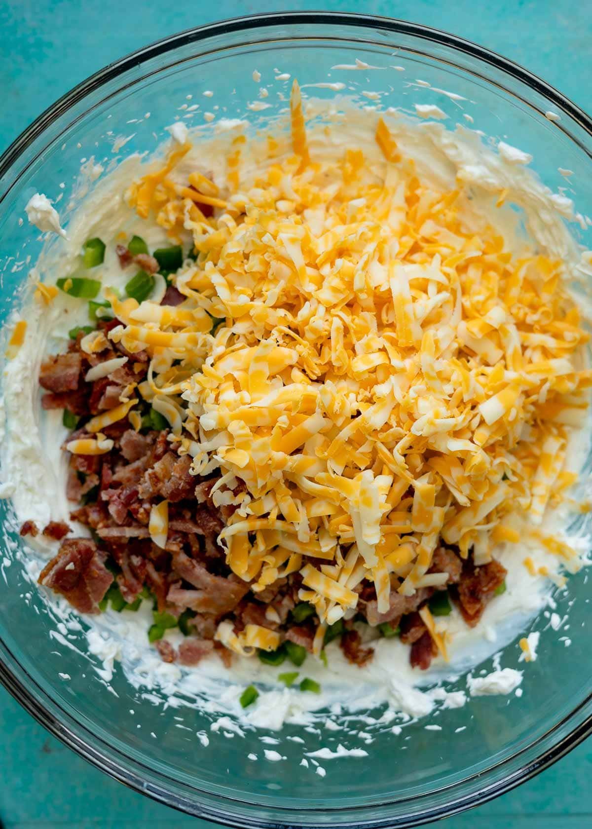 shredded cheese being added to a jalapeno popper dip
