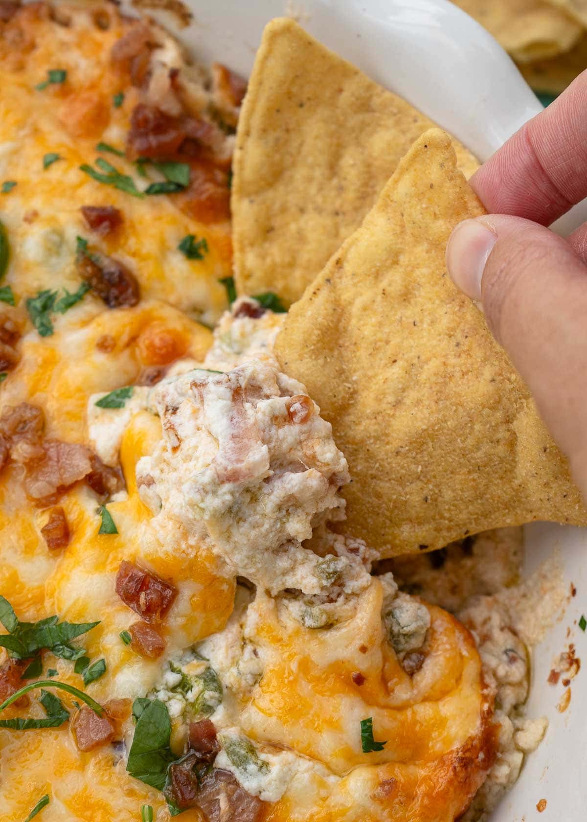 a tortilla chip scooping a big bite of jalapeno popper dip